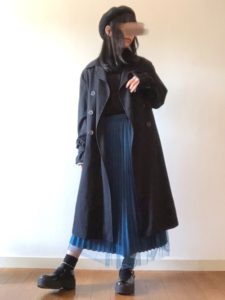 ブループリーツスカートに黒スプリングコートを着用した女性の画像